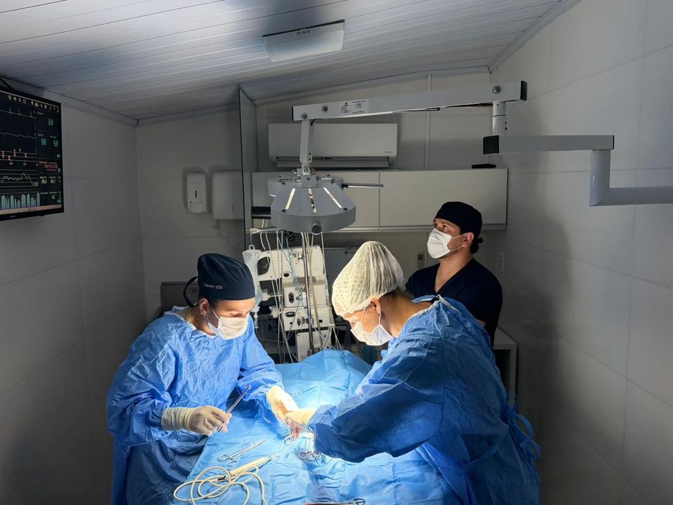 Vista do centro cirúrgico durante uma cirurgia, com monitor de sinais vitais na parede