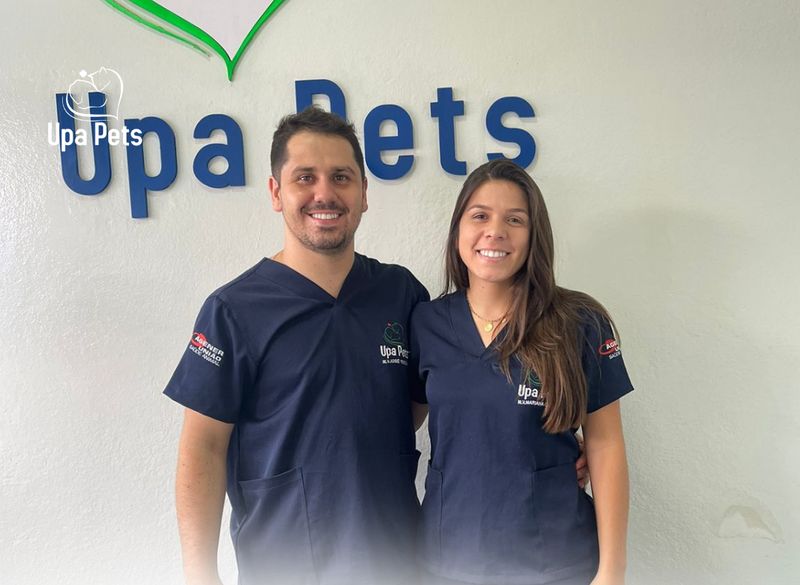 Médico Veterinário José, à esquerda, e Médica Veterinária Mariana, à direita, sorrindo em frente ao letreiro Upa Pets na clínica